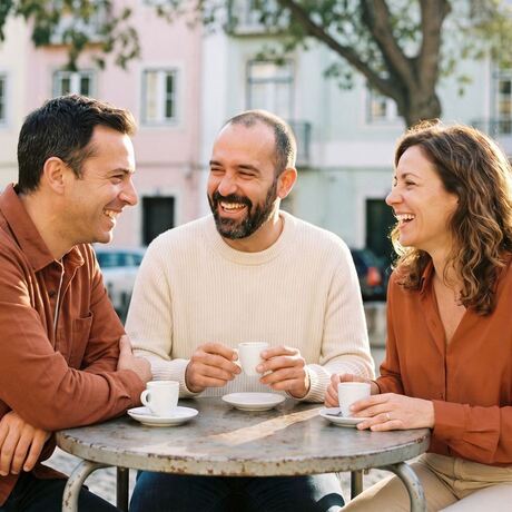 Three friends laughing at a café terrace table in Lisbon, with coffees and pastéis de nata.